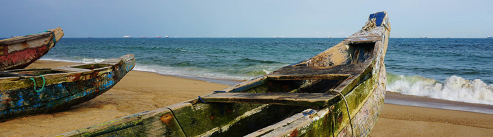Houten vissersboten op het zandstrand aan de kust van Togo, met de Atlantische Oceaan op de achtergrond.