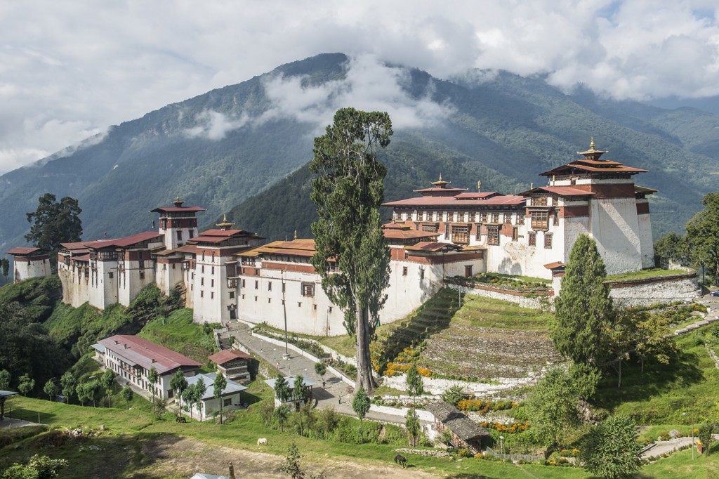 Uitzicht op het Tashichho Dzong-klooster in Bhutan, met groene Himalaya-bergen en wolken op de achtergrond.