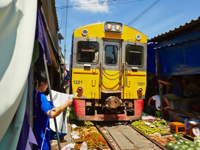 Gele trein rijdt door de Maeklong Railway Market in Thailand, langs kraampjes met fruit op het spoor.