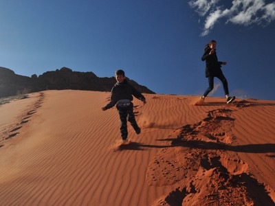 Kind en vrouw rennen door het rode zand van Wadi Rum tijdens de Route Jordanië.