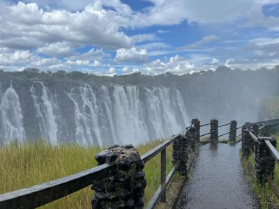 Uitzichtpunt bij Victoria Falls met watervallen en nevel onder een blauwe lucht met wolken.