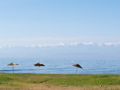 Oever van het Issyk-Kulmeer met rieten parasols en uitzicht op de besneeuwde bergen van Kirgistan.