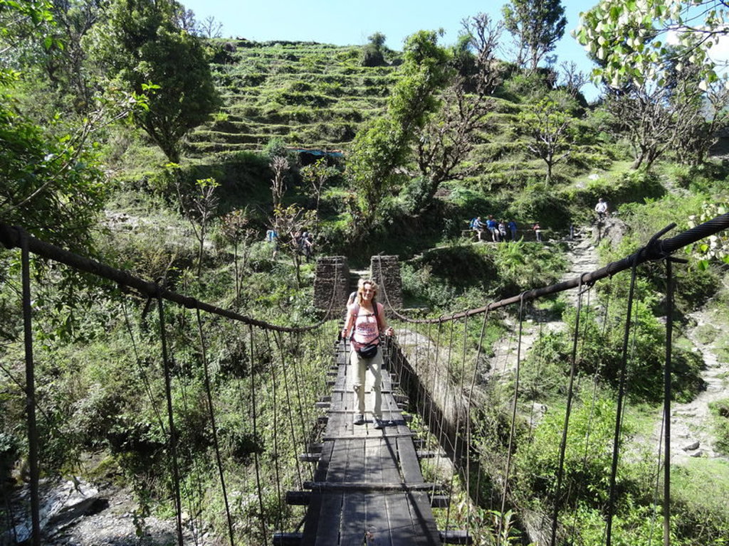 Wandelaar op hangbrug tijdens actieve groepsrondreis Nepal, met groene heuvels op de achtergrond.