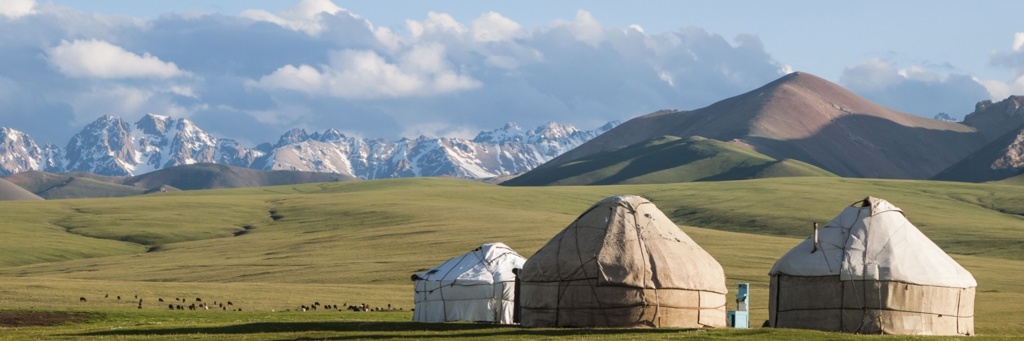 Nomadische yurts op een groene hoogvlakte met besneeuwde bergen in Kirgistan (Kirgizië).