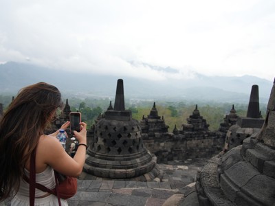 Bezoeker fotografeert Borobudur-tempel op Java met uitzicht op de omliggende heuvels.
