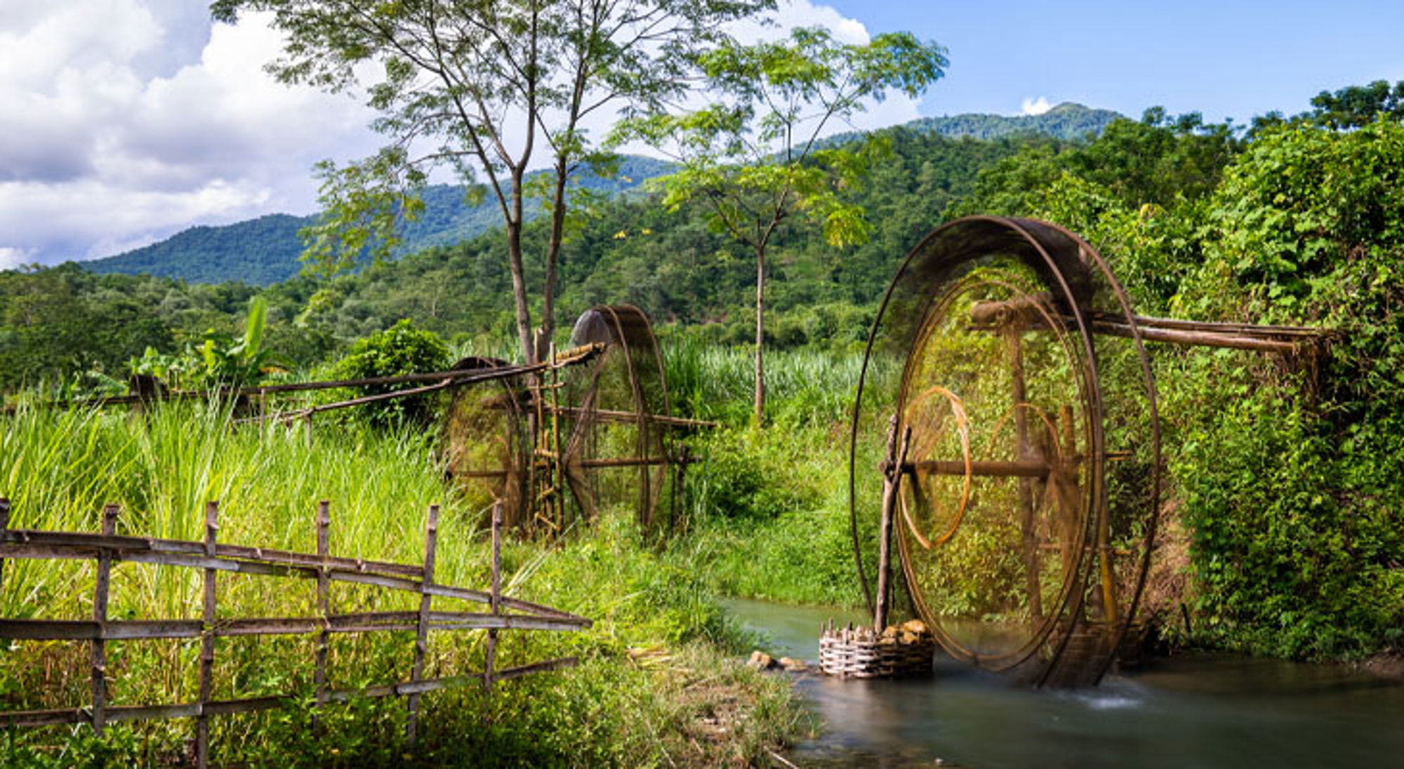 Traditionele bamboe waterwielen langs een rivier in het groene berglandschap van Vietnam.
