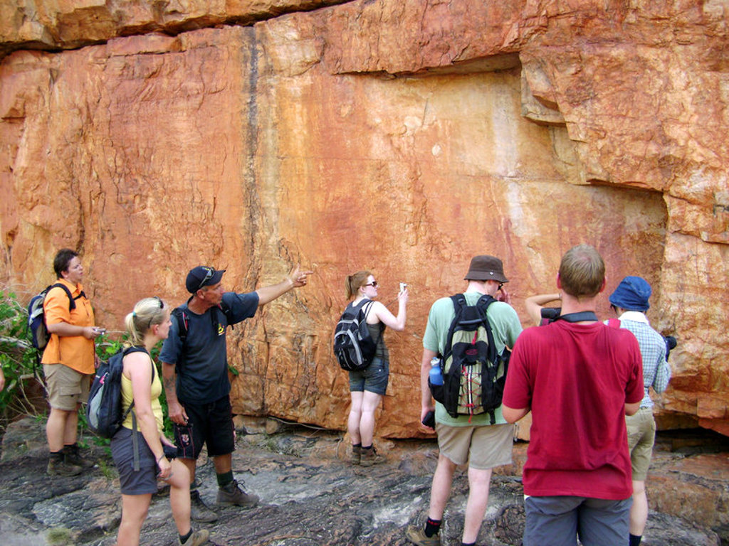 Groep wandelaars bekijkt rotswand met rotstekeningen tijdens groepsrondreis Australië van Sydney naar Darwin.
