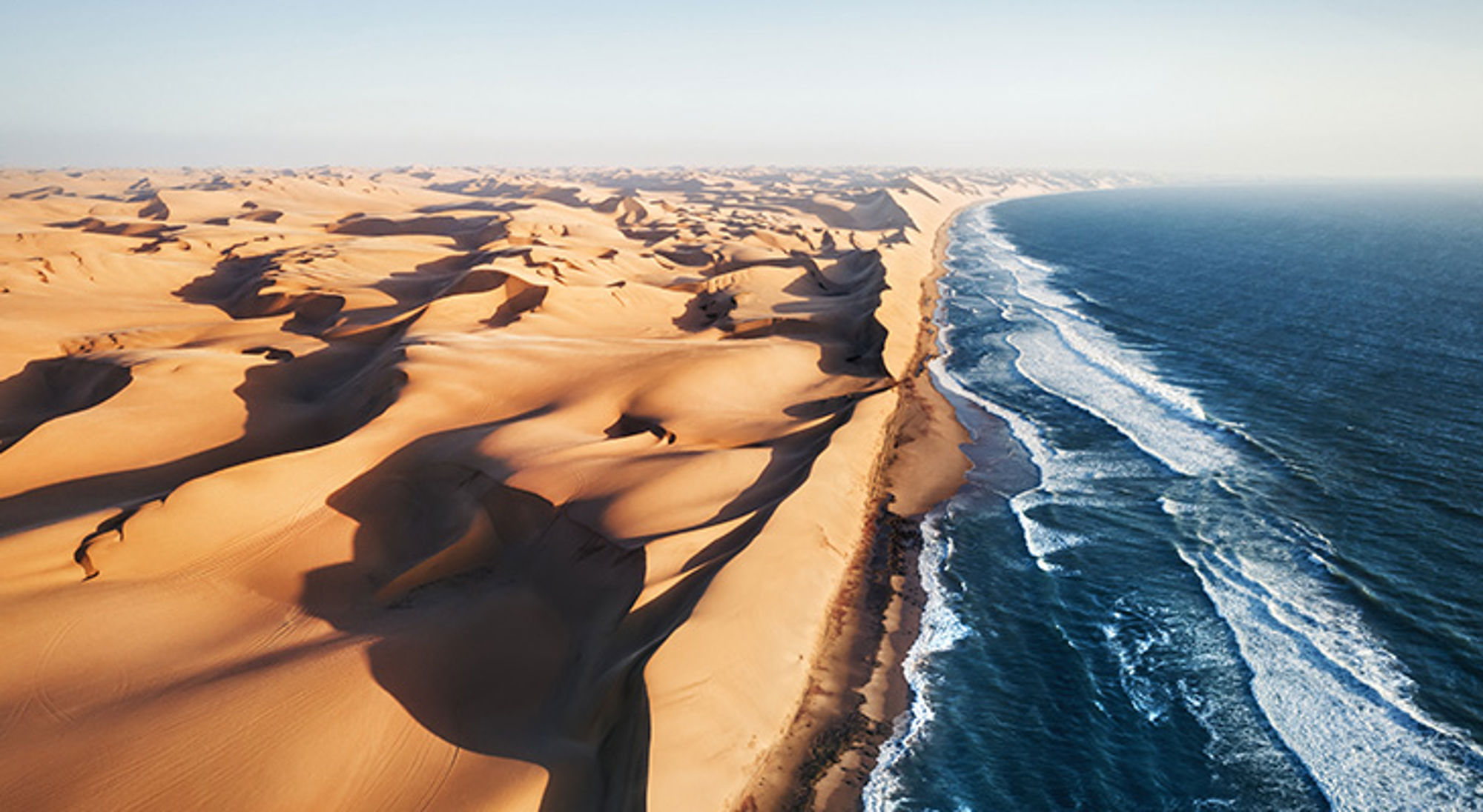 Luchtfoto van de Skeleton Coast de Namibwoestijn waar hoge zandduinen direct grenzen aan de Atlantische Oceaan in Namibië.