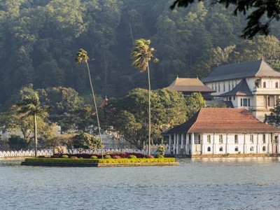 Tempelcomplex aan het meer in Kandy, Sri Lanka, met palmbomen en groene heuvels op de achtergrond.
