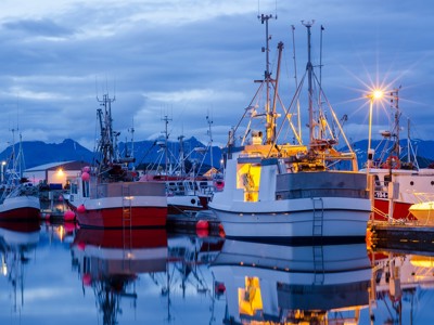 Vissersboten in een haven in Noord-Noorwegen bij schemering, met spiegeling in het stille water.