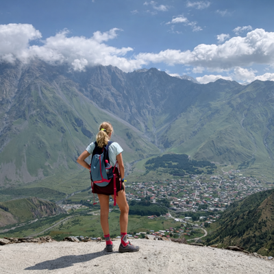 Wandelaar kijkt uit over de bergen van de Kaukasus en het dorp Stepantsminda in Georgië.