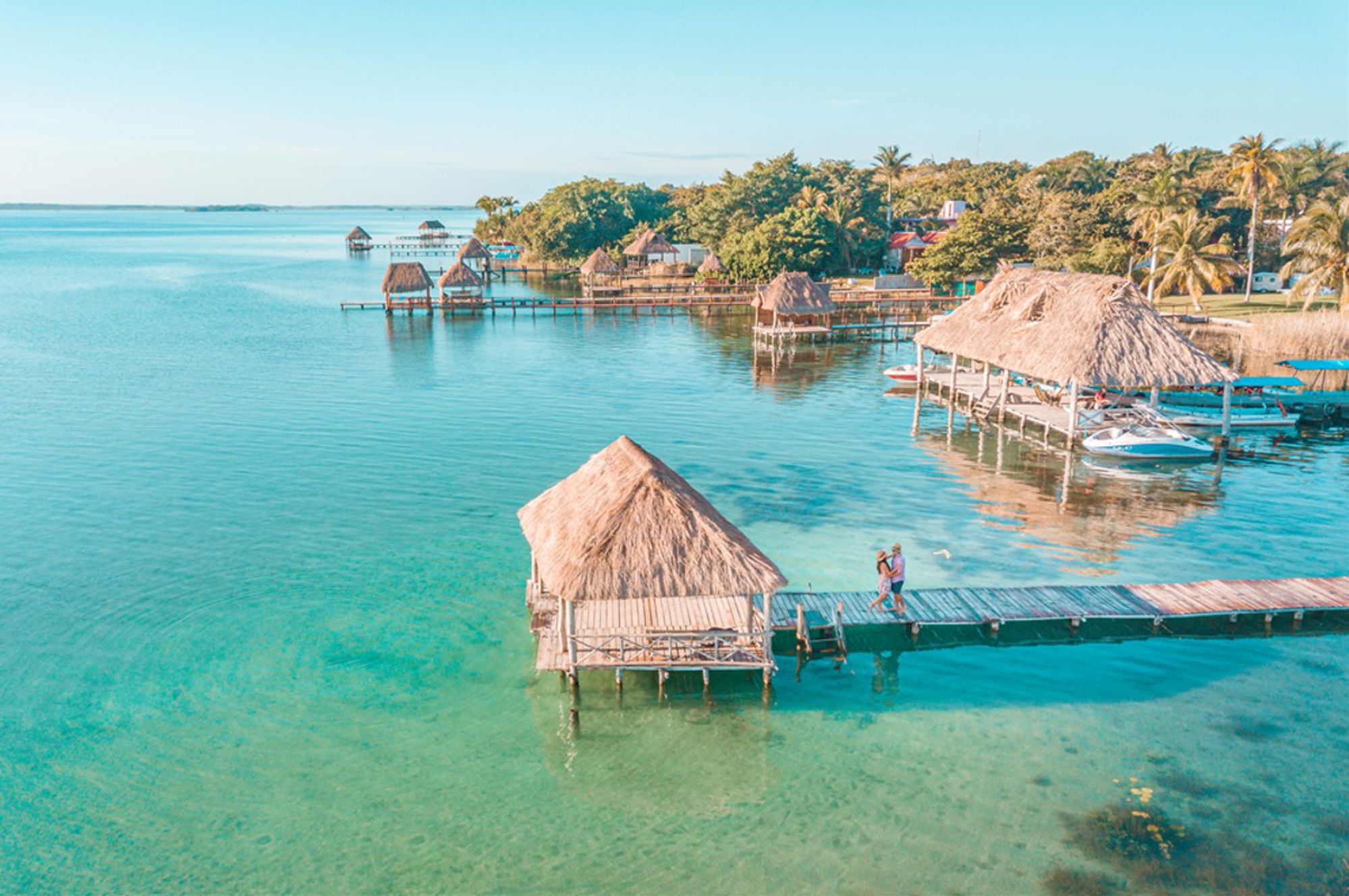 Houten pier met palapa’s boven helderblauw water bij Bacalar Lagoon in Mexico.