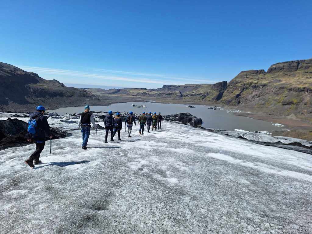 Wandelaars met helmen op een gletsjer bij een gletsjermeer in IJsland tijdens groepsrondreis IJsland.