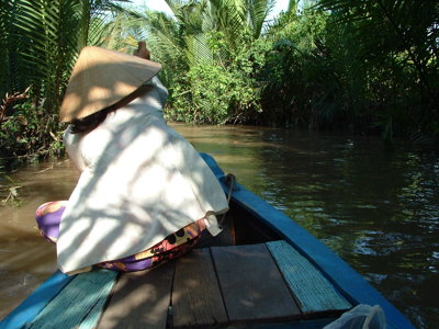Boottocht door de Mekongdelta in Vietnam, met een roeister in een traditionele hoed tussen palmen.
