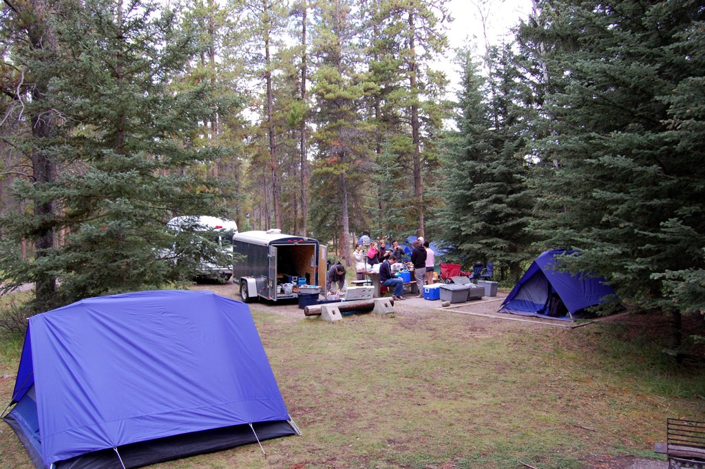 Kampeerplek in Canada West met tenten en groep reizigers bij de picknicktafel in het bos.