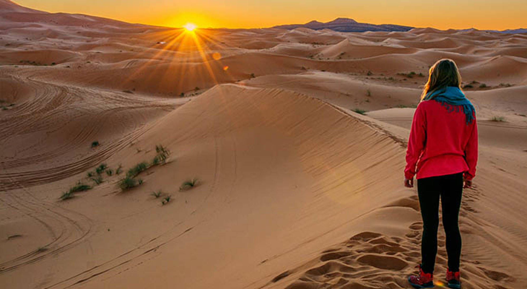 Reiziger kijkt naar zonsopkomst boven de zandduinen van de Sahara in Marokko.