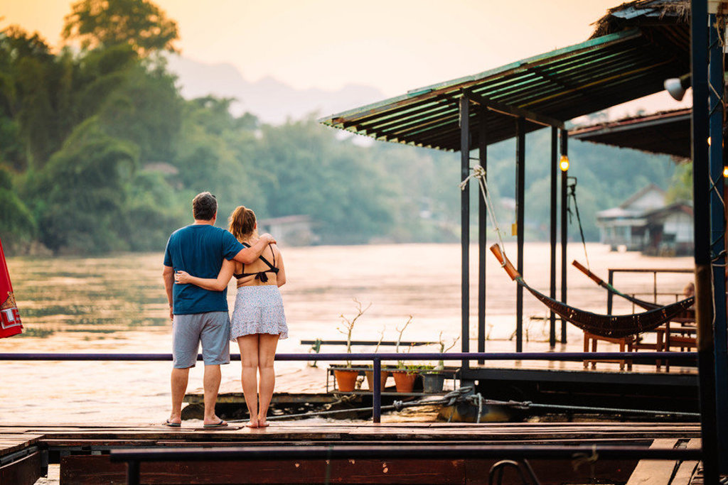 Gezin geniet van zonsondergang aan de rivier bij een drijvend terras in Thailand tijdens een familiereis.