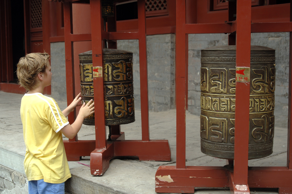 Jongen draait gebedsmolen bij een tempel tijdens familiereis China.