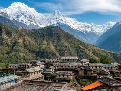 Traditioneel bergdorp in Nepal met terrassen en besneeuwde Himalaya-toppen op de achtergrond.