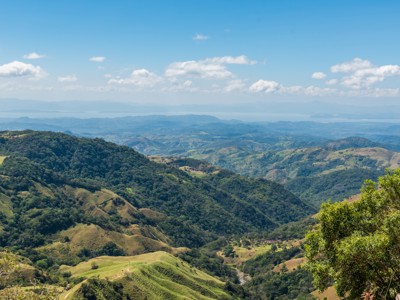 Panoramisch uitzicht over groene bergketens en valleien in Costa Rica, onder een blauwe lucht met wolken.