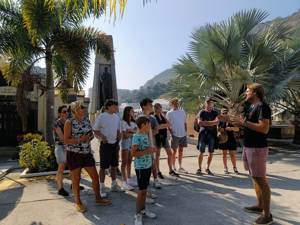 Gezelschap tijdens familiereis Argentinië en Brazilië krijgt uitleg van gids bij monument tussen palmbomen.