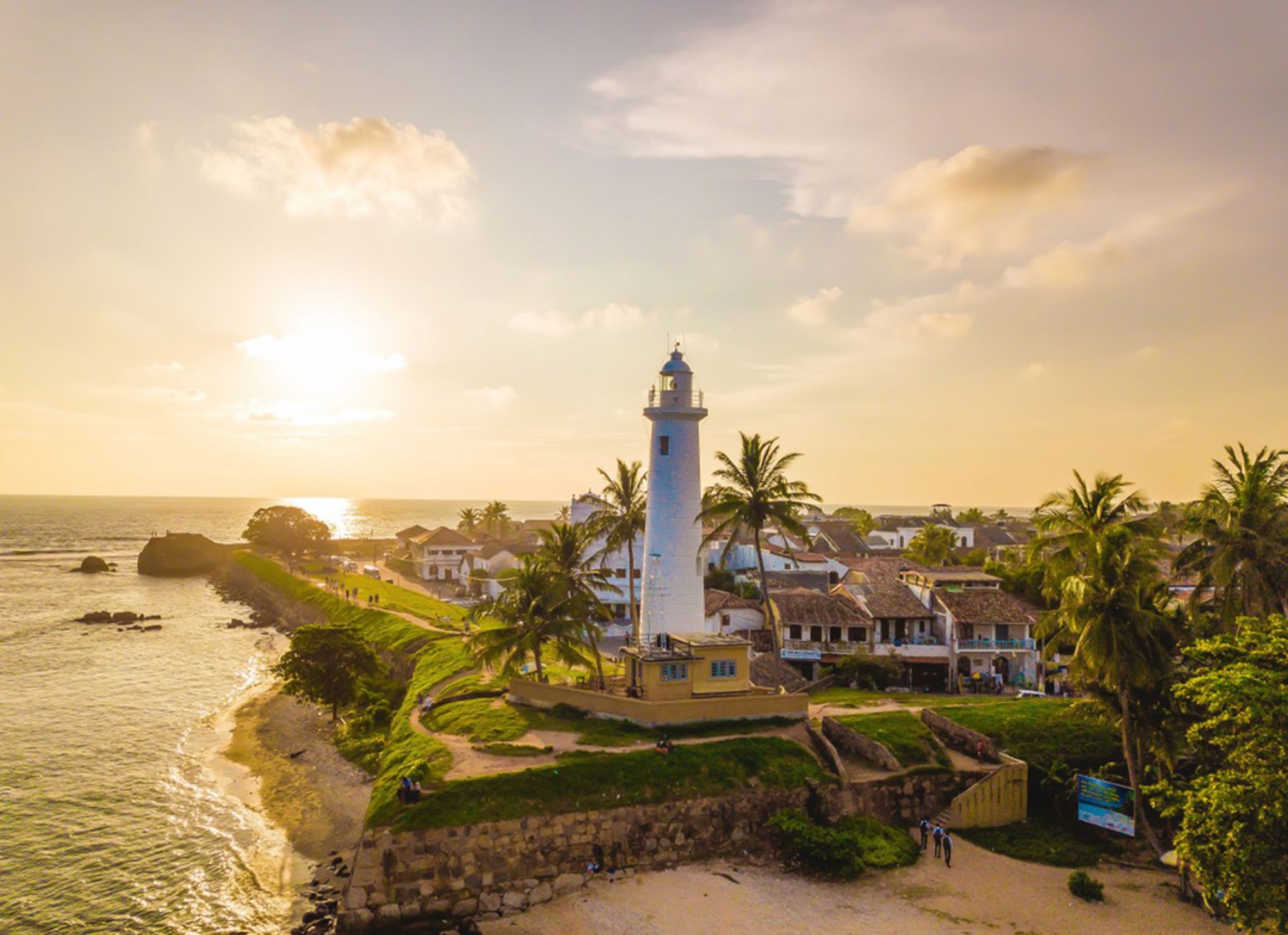 Vuurtoren van Galle bij zonsondergang aan de kust van Sri Lanka, omringd door palmbomen en oude stadsmuren.