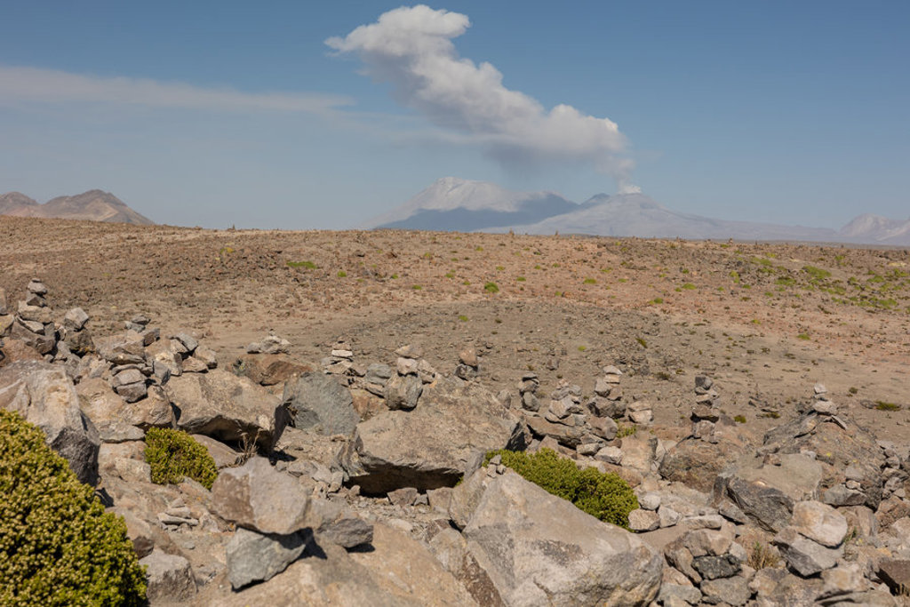 Rotsachtig woestijnlandschap in Peru met rokende vulkaan onder een blauwe lucht.