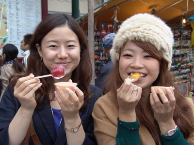 Twee vrouwen proeven Japanse streetfood-snoepjes op een markt tijdens de Route Japan.