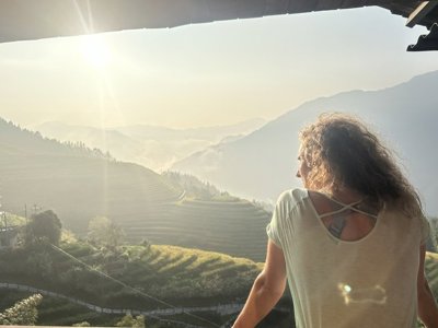 Reiziger kijkt uit over rijstterrassen en bergen in China tijdens groepsrondreis, bij zonsopkomst.