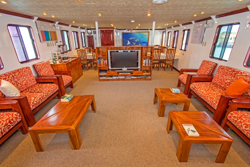 Lounge van het expeditieschip tijdens de groepsrondreis Galapagoseilanden, met zitbanken, tafels en eethoek.