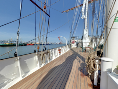 Dek van een zeilschip in de haven van Antigua, met zicht op de kade en aangemeerde schepen.