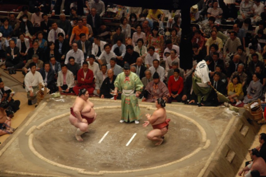 Sumoworstelaars in de ring tijdens een wedstrijd, omringd door publiek in Japan.