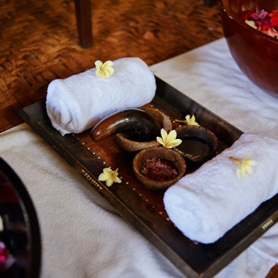 Massage in Labuan Bajo: handdoeken, aromatische olie en bloemen op een houten dienblad.