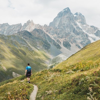Wandelaar op bergpad met uitzicht op de hoge bergen van Georgië tijdens een 22-35ers reis.