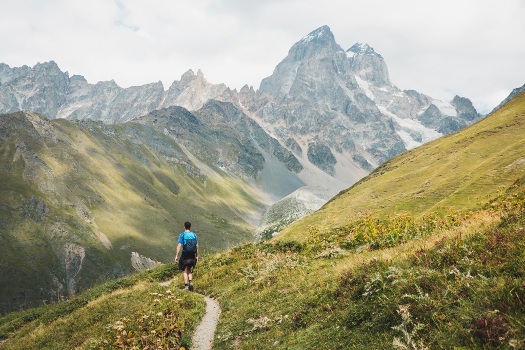Wandelaar op bergpad met uitzicht op de hoge bergen van Georgië tijdens een 22-35ers reis.