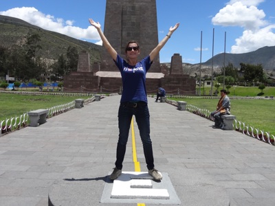 Reiziger bij het Mitad del Mundo-monument op de evenaar in Ecuador, met armen omhoog.