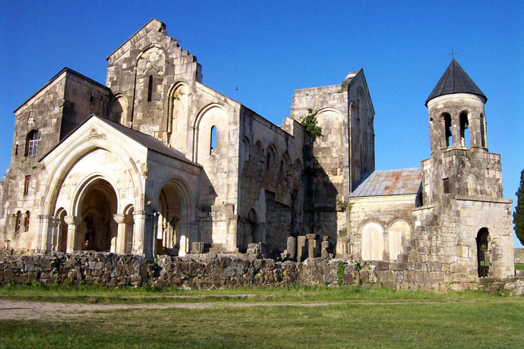 Middeleeuws kloostercomplex Gelati bij Koetaisi, Georgië, met stenen kerk en klokkentoren onder blauwe lucht.