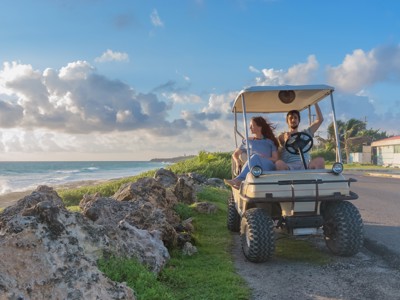 Twee reizigers in een golfkar langs de kustroute in Mexico bij zonsondergang.