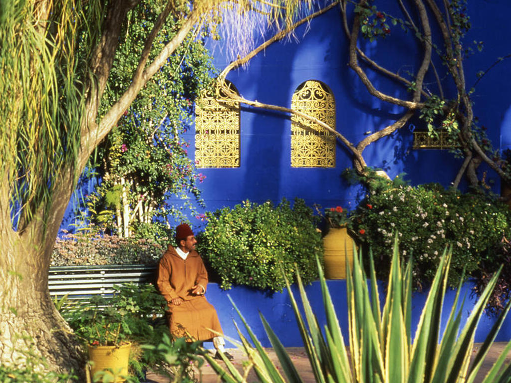 Man in traditionele kleding in de tuin bij de blauwe Majorelletuin in Marrakech, Marokko.