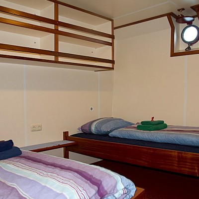 Comforthut met stapelbed, opgemaakt beddengoed en patrijspoort op een schip.