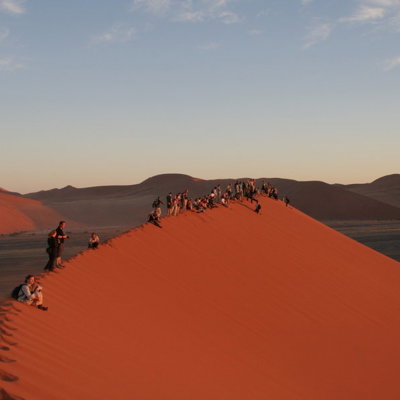 Reizigers op een rode zandduin in de Namib-woestijn tijdens een groepsrondreis Namibië.
