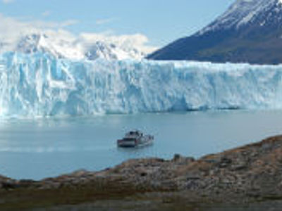 Boot vaart langs een gletsjer in een fjord, met besneeuwde bergen op de achtergrond.