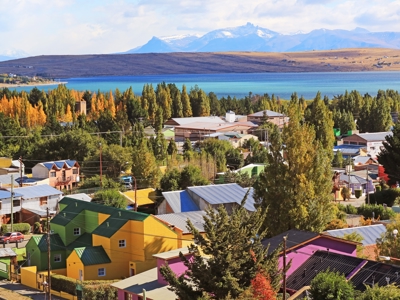 Kleurrijke huizen aan een azuurblauw meer met besneeuwde bergtoppen in Patagonië.