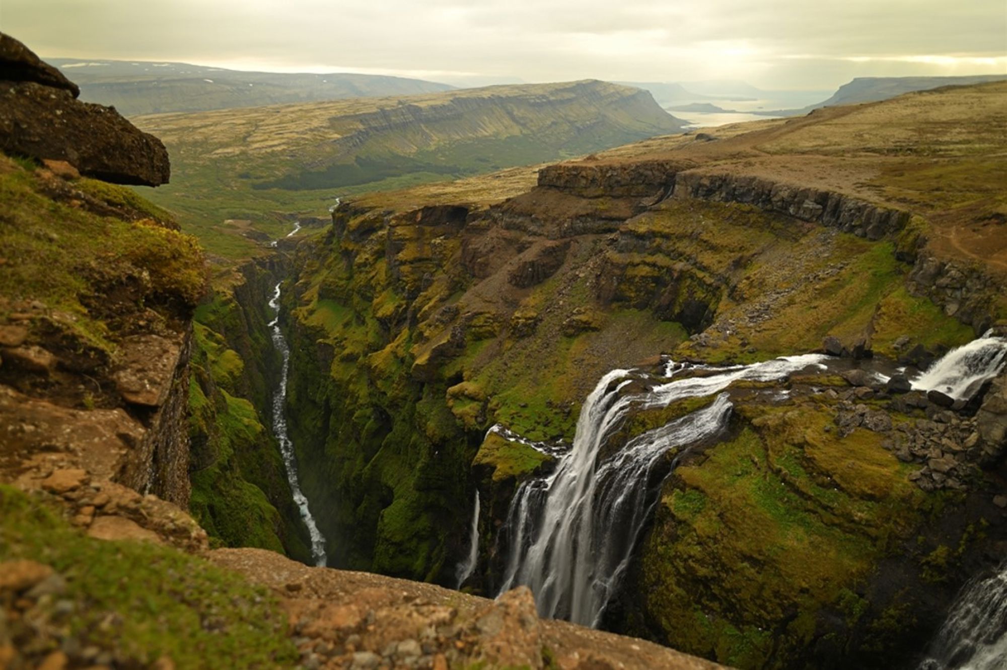 Waterval die in een groene kloof stroomt in het ruige landschap van IJsland.