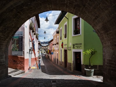 Straat in historisch Quito, Ecuador, met kleurrijke gevels onder een stenen boog en een man op een ladder.