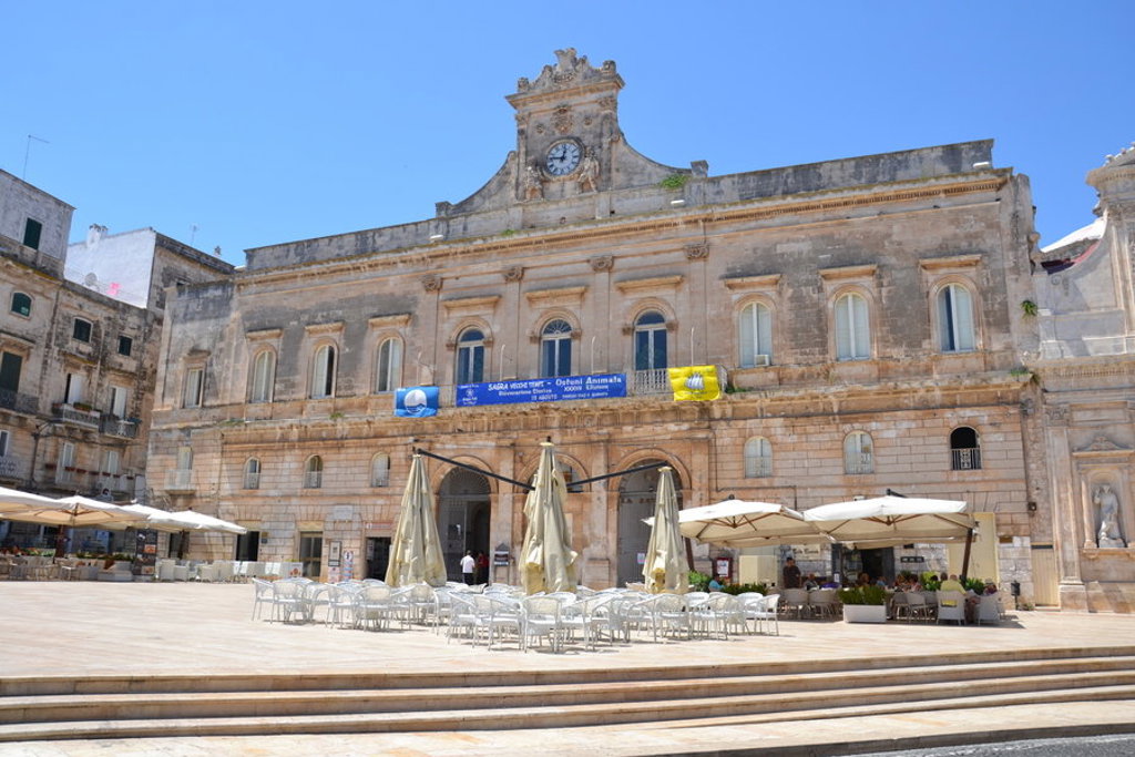 Historisch stadhuis met klok aan een plein met terrassen in Puglia, Italië.
