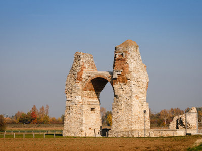 Romeinse ruïne met stenen boog langs de Donau-fietsroute, met herfstbomen op de achtergrond.