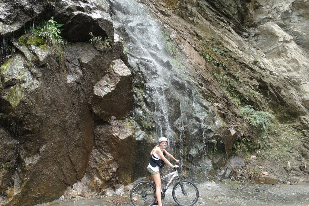 Fietser bij een waterval langs een rotswand in Ecuador tijdens een groepsrondreis.