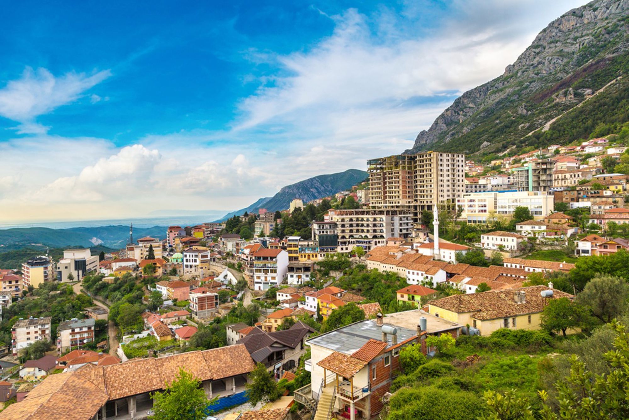 Panoramisch uitzicht op Krujë in Albanië, met huizen op de heuvel en bergen onder een blauwe lucht.