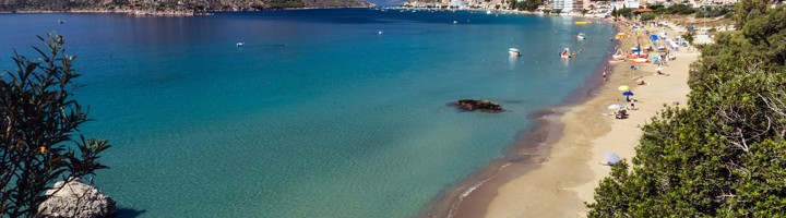 Panoramisch uitzicht op het zandstrand en de baai van Tolo, Griekenland, met helderblauw water en bergen.